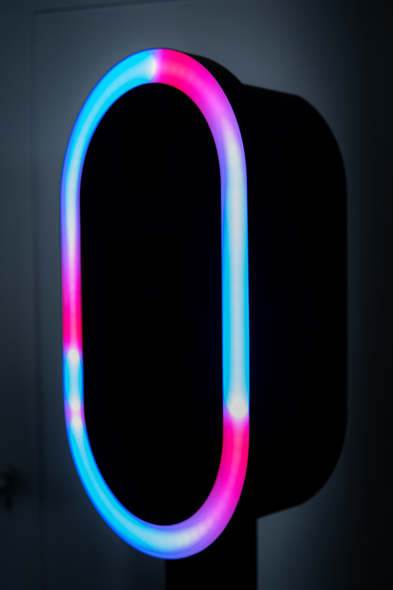 Illuminated mirror with a glowing frame displaying gradients of blue, pink, and purple colors against a dark background.